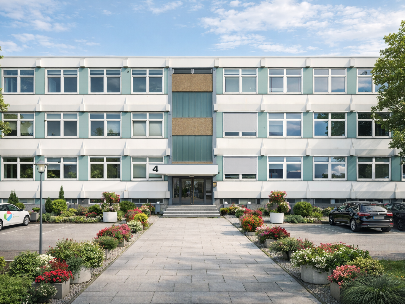 Dreistöckiges Bürogebäude mit zentralem Eingang, Blumenbeeten und Parkplätzen